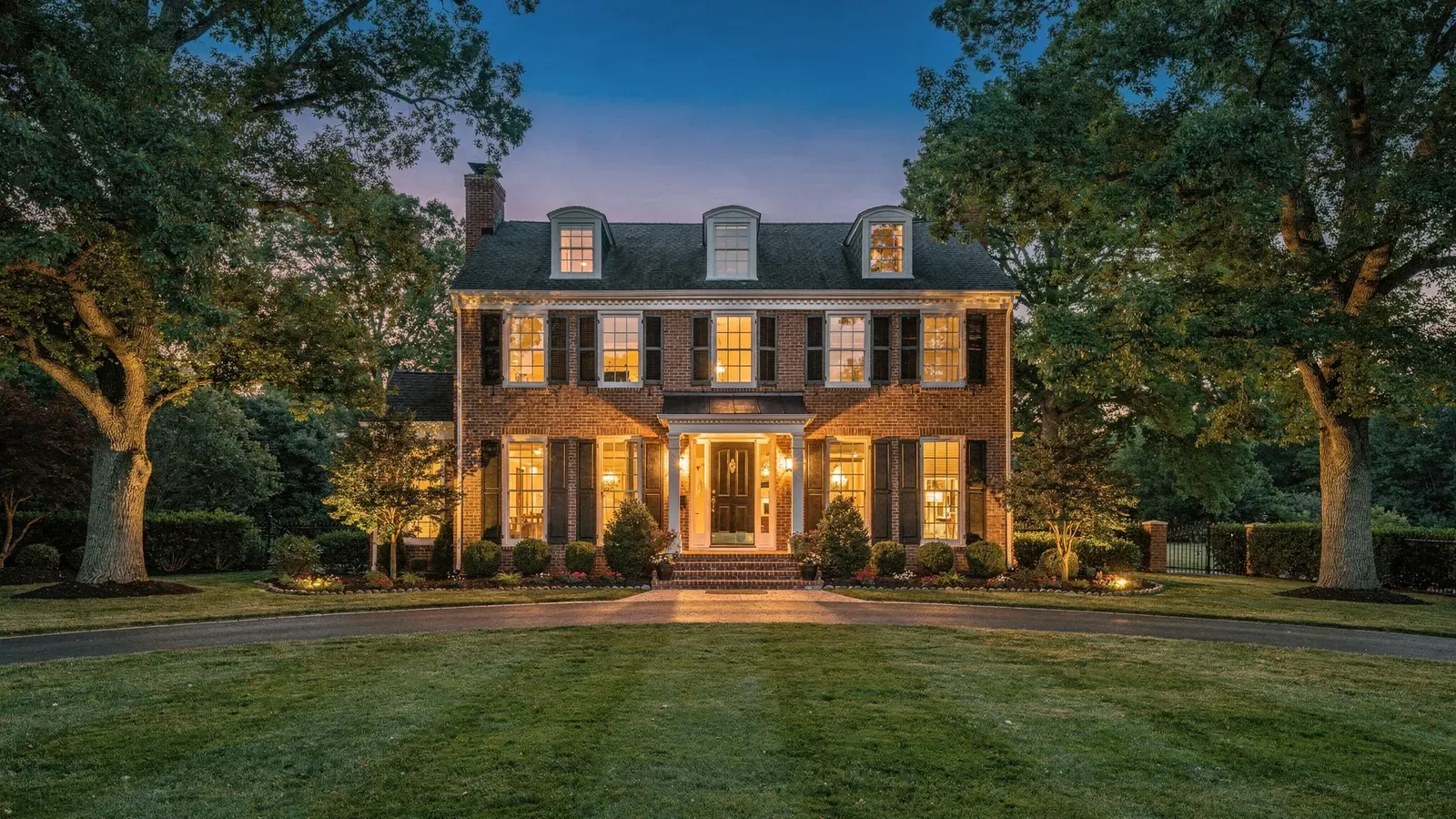 A brick colonial at dusk, its windows lit. A generated picture, not a listing.